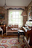 Two seater sofa at window of London home with piano and lamp England UK
