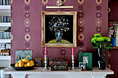 Ornaments and homeware with bowl of lemons set against patterned wallpaper on mantlepiece in London home UK