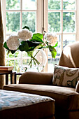 Cut flowers and sunlit armchair and footstool at doorway in West London townhouse England UK