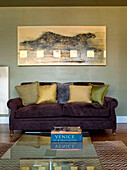 Goldene Kissen auf lilafarbenem Sofa unter einem Kunstwerk mit Leopardenmotiv und einem Couchtisch mit Glasplatte in einer Londoner Wohnung England UK