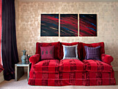 Triptychon über rot gestreiftem Sofa in goldfarbenem gedämpftem Metallic-Wohnzimmer in Londoner Wohnung England UK