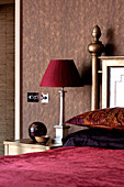 Dark pink lamp and bed cover on metallic gold bed in bedroom of London apartment England UK