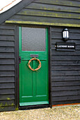 Bright green door to creosoted laundry room in grounds of rural Suffolk home England UK