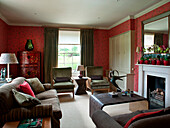 Sofas und Regal im rot tapezierten Wohnzimmer mit lackiertem chinesischem Schrank in einem Landhaus in Suffolk, England UK
