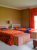 Orangefarbene Bettbezüge in einem Zweibettzimmer mit gepolsterten Deckenkästen in einem Haus im ländlichen Suffolk, England, UK