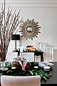 Dining room detail with large twig arrangement and sola burst mirror in Paris apartment, France