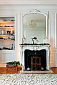 Mirror on marble fireplace with birdcage and recessed shelving at Christmas, in Paris apartment, France
