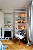 Armchair at fireplace with lit candles on shelving unit in bedroom of Paris apartment, France