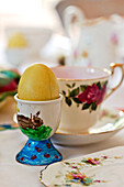 Easter egg in hand-painted eggcup with teacup in Essex home, England, UK