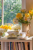Teetassen und Schnittblumen auf der sonnenbeschienenen Fensterbank eines Hauses in Essex, England, Vereinigtes Königreich