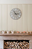 Roman numerals on clock face above stone fireplace with cupcakes and crockery, Buckinghamshire home, England, UK