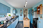 Wooden island unit in fitted blue kitchen of Bovey Tracey family home, Devon, England, UK