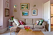 Kunstwerke über dem hellbraunen Sofa im rosa Wohnzimmer des Hauses der Familie Bovey Tracey, Devon, England, UK