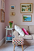 Kunstwerke über einem braunen Sofa mit gepolstertem Fußhocker im Wohnzimmer eines Familienhauses in Bovey Tracey, Devon, England, UK
