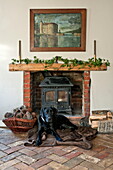 Black dog sits on floor in front of wood burning stove in living room of Suffolk farmhouse, England, UK