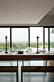 Wooden dining table with bench seats and view of countryside from contemporary detached home, Cornwall, England, UK