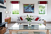 Schnittblumen auf einem gläsernen Couchtisch mit Sofa und Kunstwerken in einem modernen Haus in Cornwall, England, UK