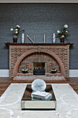 Mirrored coffee table in front of brick fireplace in living room of London home, England, UK