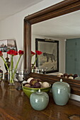 Cut flowers and ornaments on sideboard with wooden framed mirror in contemporary Suffolk country house, England, UK