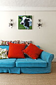 Brightly coloured sofa and cushions below artwork of cow in contemporary Suffolk/Essex home, England, UK