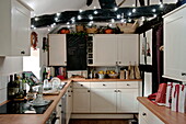 Lichtspiele an der Balkendecke in der weißen Einbauküche eines Cottage in Shropshire mit eingepackten Geschenken, England, UK