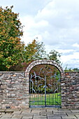 Arched metal garden gate in farmhouse garden, Blagdon, Somerset, England, UK