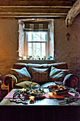 Zweisitzer-Sofa mit Obstkorb unter dem Fenster im Balken-Wohnzimmer eines Hauses in Tregaron, Wales, UK
