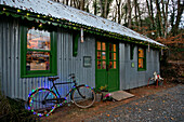 Bicycle with fairylights at exterior of corrugated metal shop with green paintwork in Tregaron Wales UK