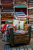 Crochet blankets and cushion on worn leather armchair with shelves of Welsh blankets in Tregaon shop interior Wales UK