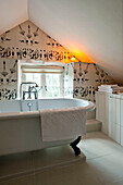 Freestanding roll-top bath with patterned wallpaper in attic bathroom of Sherford barn conversion Devon UK