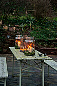 Lit candles and large storage jars on weathered table Sherford garden terrace Devon UK