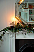 Lit candle with octagonal mirror and festive garlands on mantlepiece in Crantock home Cornwall England UK