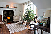 Rocking chair beside Christmas tree with lit wood burning stove in Crantock home Cornwall England UK