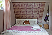 Patterned wallpaper above double bed with pink blanket and curtains in East Grinstead family home West Sussex England UK