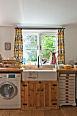 Spülbecken und Holzschrank mit Waschmaschine unter dem Küchenfenster eines Hauses in Cambridge, England, UK