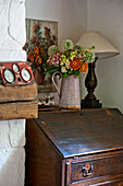 Lamp and cut flowers on vintage wooden writing bureau in Cambridge cottage England UK