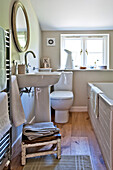 Circular mirror above pedestal basin with low stool in Cambridge cottage bathroom England UK