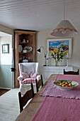 Wooden corner cabinet and wingback armchair with kitchen table in beach house kitchen Cornwall England UK