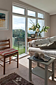 Striped cushion on wooden chair with knitting at window in sunlit beach house Cornwall England UK