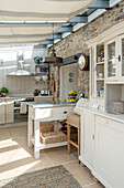 White kitchen dresser with exposed stone wall in kitchen extension of Penzance farmhouse Cornwall England UK