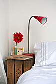 Red lamp and single stem Chrysanthemum flower on wooden crate at bedside in family townhouse Cornwall England UK