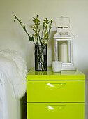 Cut flowers and hurricane lantern on lime green drawers in summerhouse UK