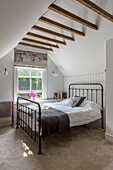 Metal framed bed at sash window below high beamed ceiling in Tunbridge Wells home Kent England UK