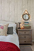 Circular mirror with fairylights above chest of drawers at bedside in Penzance farmhouse Cornwall UK