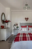 Herzförmiges Ornament über einem Doppelbett mit rot-weiß karierter Decke in einem Bauernhaus in Penzance, Cornwall, UK