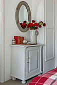 Red cut flowers and circular mirror in sideboard in Penzance bedroom Cornwall UK