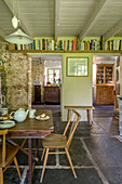 Wooden chair at table in kitchen with bookshelf above doorways in Helston farmhouse Cornwall UK