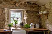 Exposed stone farmhouse kitchen with spray tap at Belfast sink at window in Helston Cornwall UK