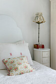 Upholstered lamp on bedside table with floral cushion and pillow with monogram in Marazion beach house Cornwall UK