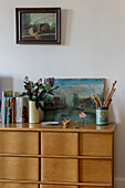 Vintage-Stricknadeln, geschnittene Blumen und Kunstwerke auf Holzschubladen in einem Londoner Schlafzimmer UK